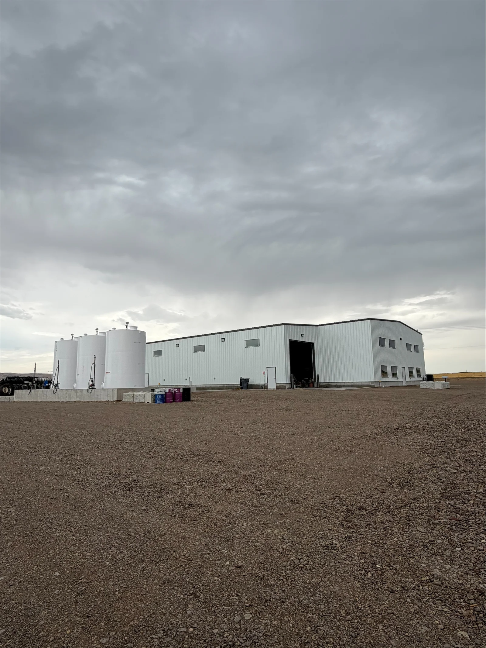 Metal warehouse building with three white storage tanks and electrical infrastructure installation