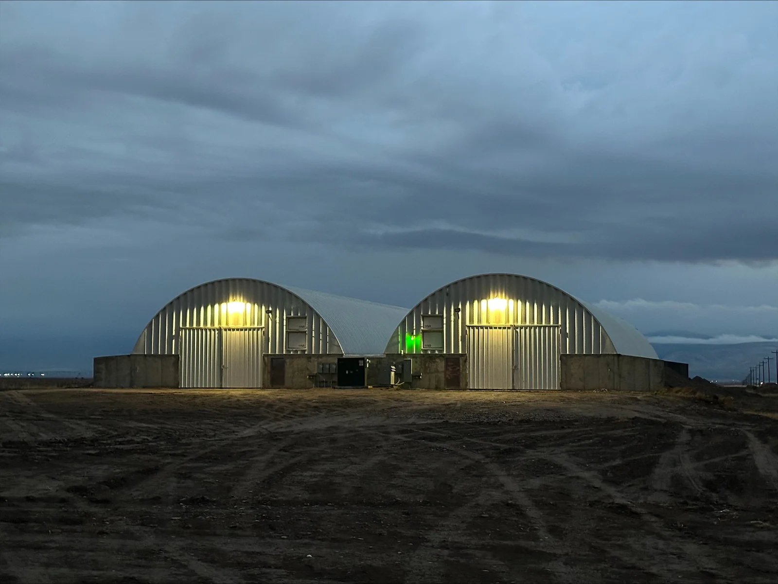 Two illuminated corrugated metal agricultural buildings with interior LED lighting at dusk
