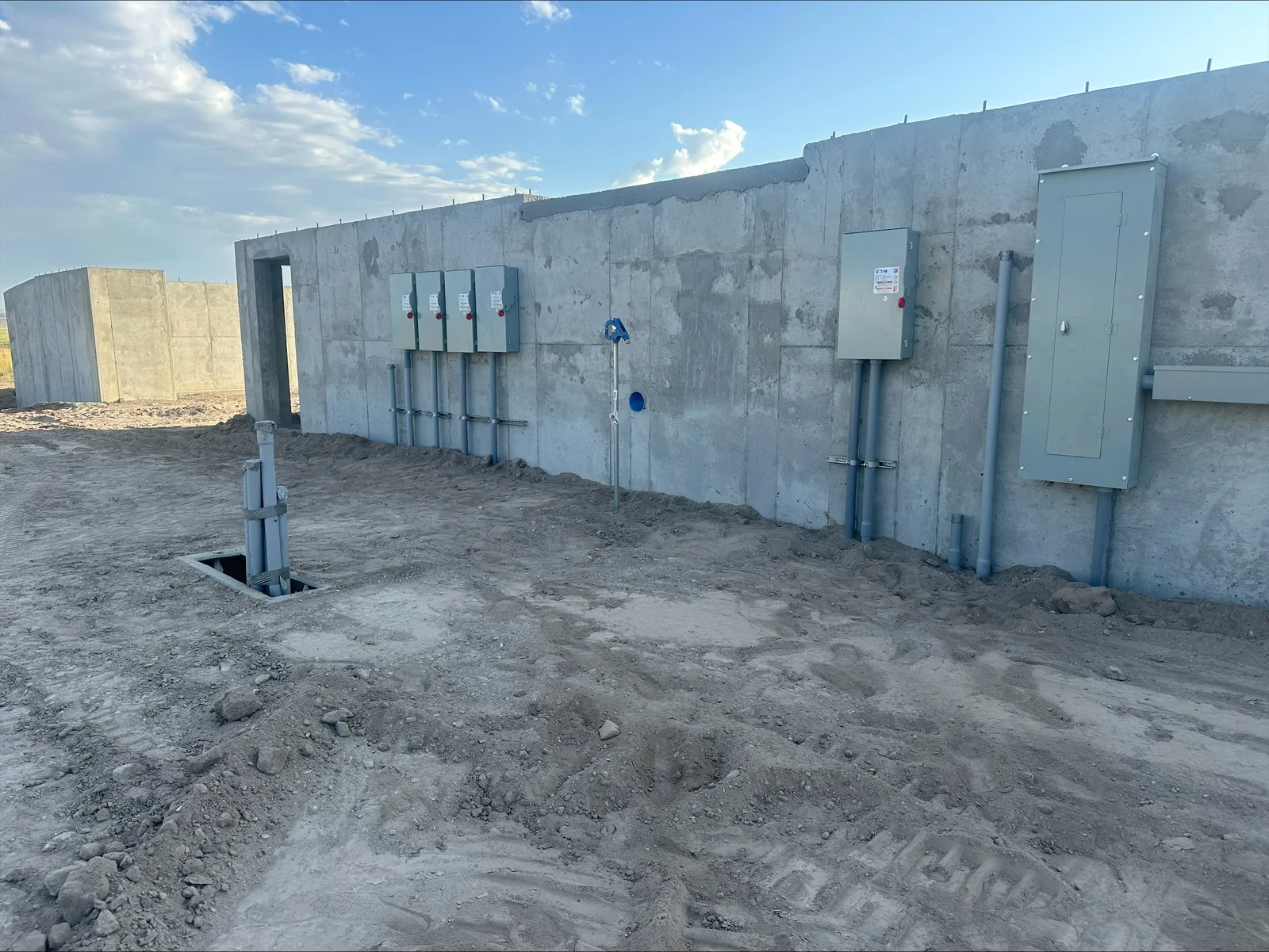 Concrete pad with mounted electrical panels, disconnects, and conduit installations on precast walls