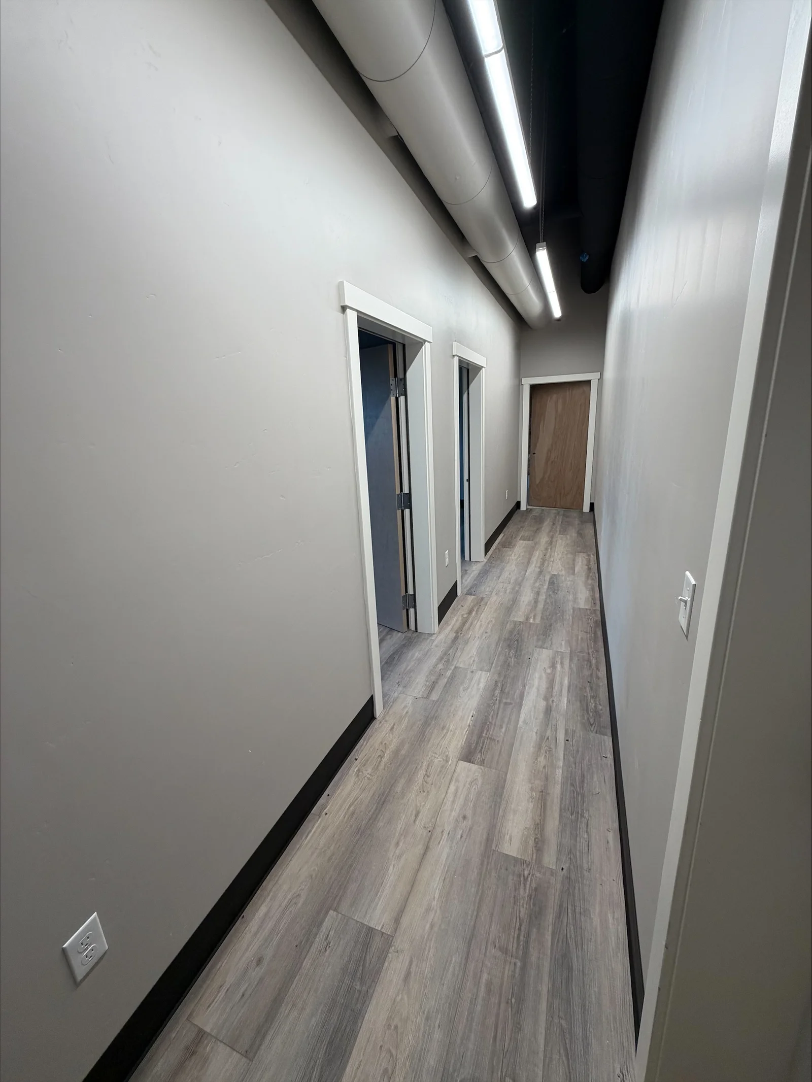 Hallway with recessed linear LED ceiling lights, white walls, and gray vinyl plank flooring
