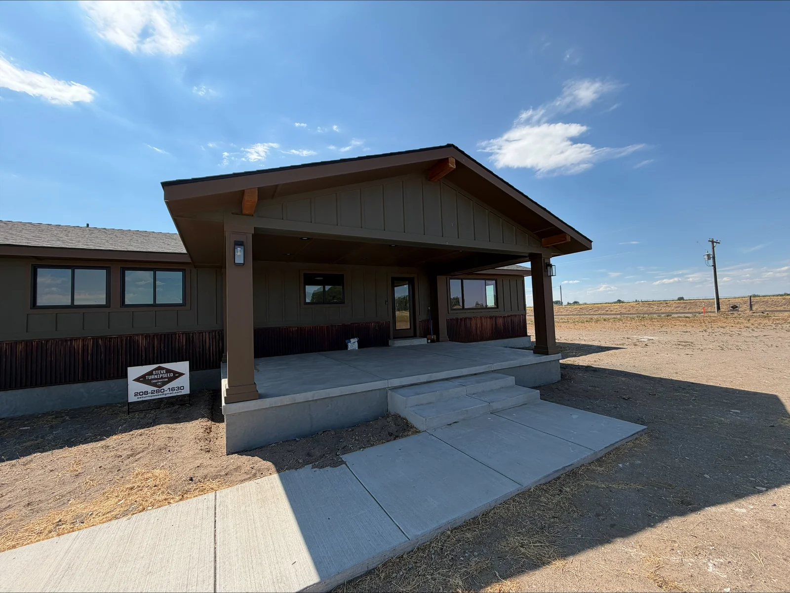 New home with board-and-batten exterior, metal roof, covered porch, and concrete walkway