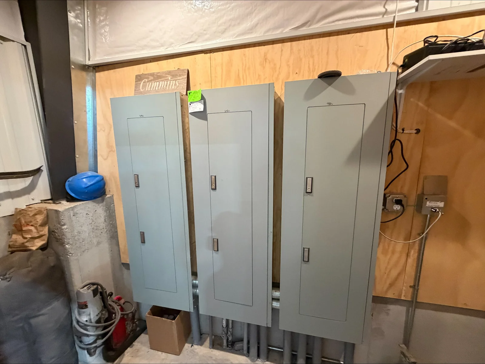 Three gray electrical panels with disconnect switches mounted on metal frame in commercial space