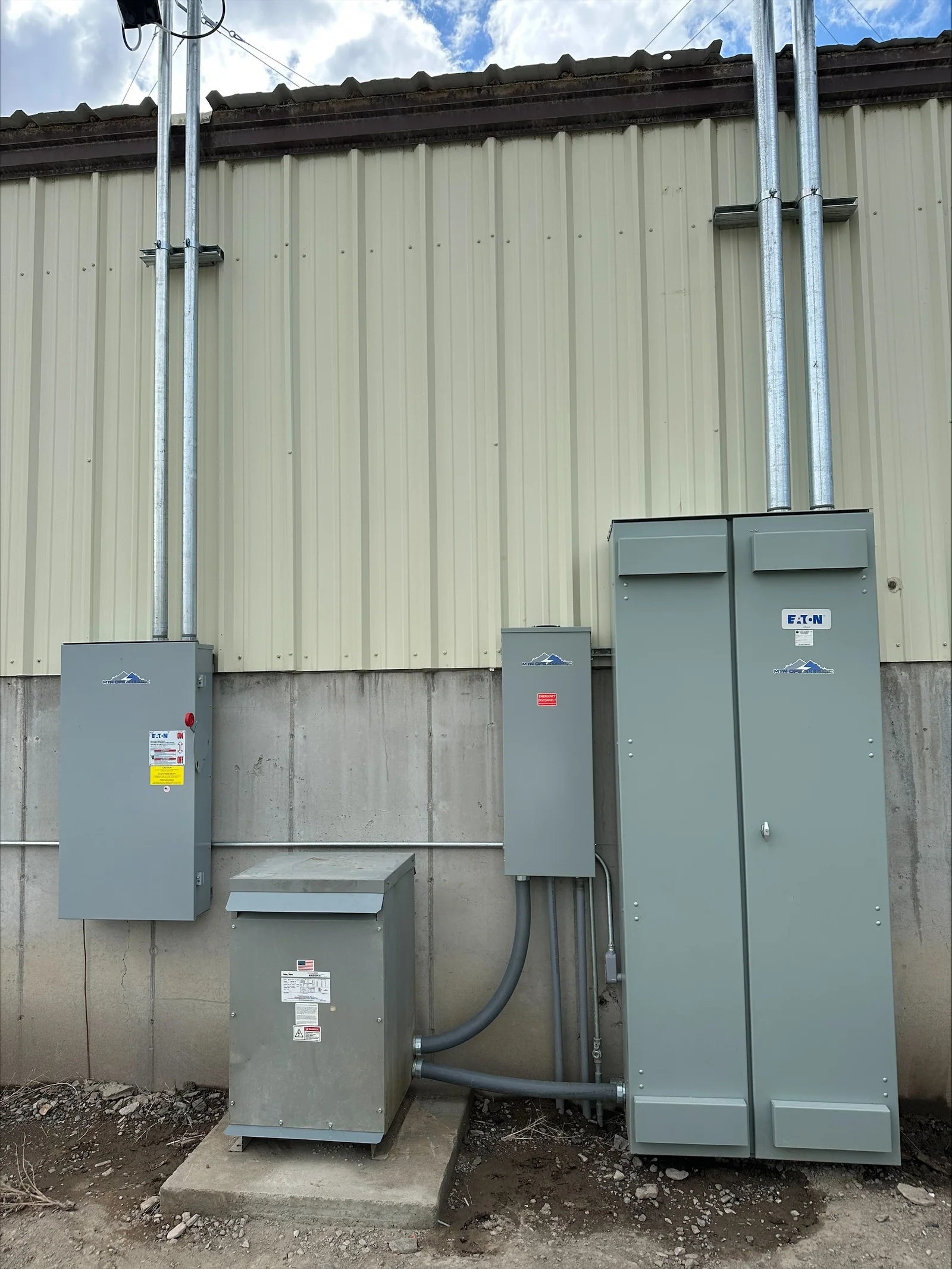 Gray electrical panels and transformer mounted on concrete foundation with conduit runs and safety labels